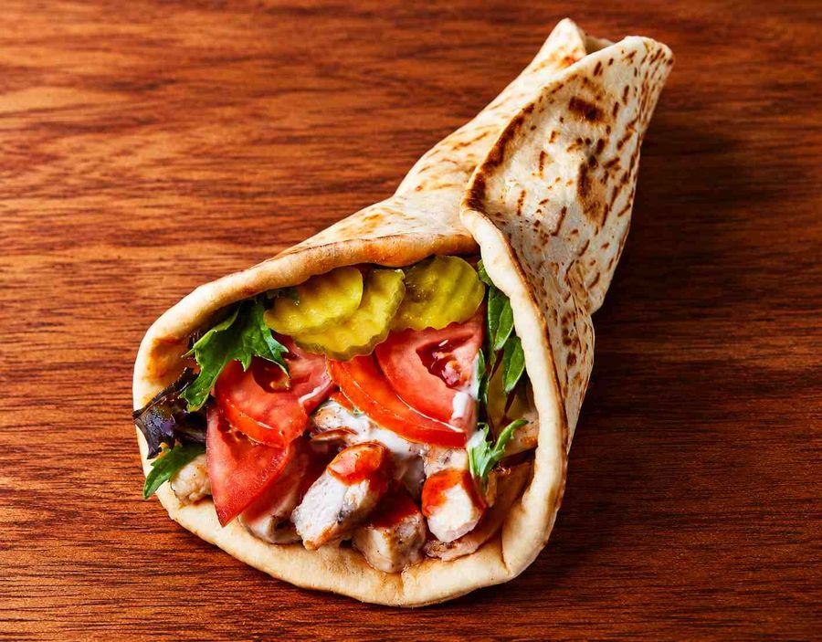 A pita wrapped around grilled chicken, tomato, lettuce, pickles and white sauce.