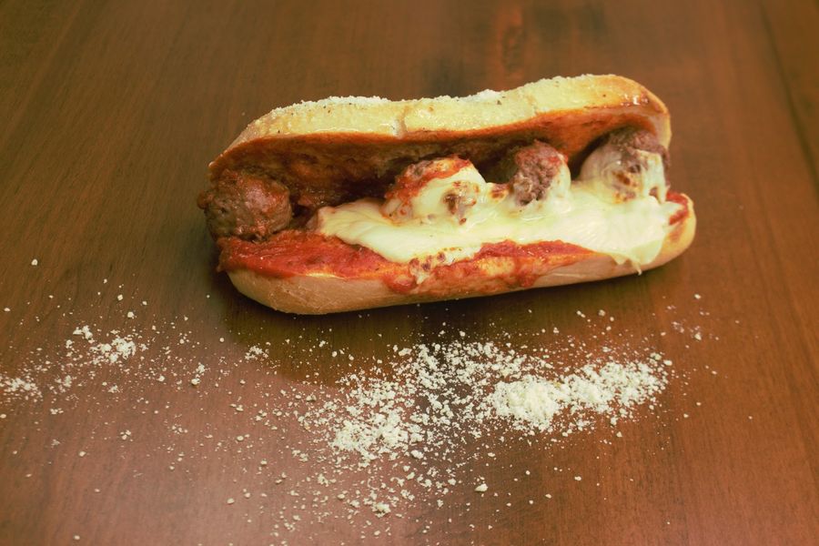 A sub roll filled with meatballs in red sauce and melted white cheese, with grated parmesan scattered on the table.
