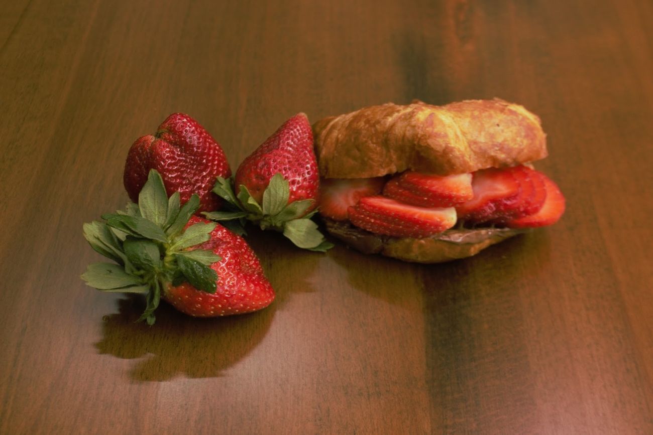 A croissant spread with chocolate and filled with sliced strawberries, with three whole strawberries beside it.